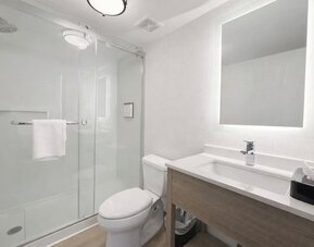 Contemporary guest bathroom featuring a walk-in glass shower, modern vanity, illuminated mirror and fresh towels at Hyatt Select Philadelphia Airport.