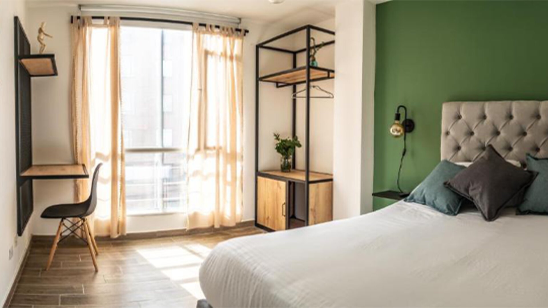 Guest room at 103 Wonderful House featuring a comfortable bed, green accent wall, workspace and large windows with natural light.