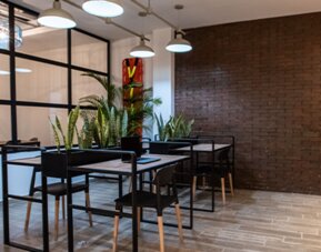 Communal dining area at 103 Wonderful House featuring modern tables, bar seating, indoor plants and exposed brick accents.
