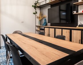Meeting and seating area at 103 Wonderful House featuring a large wooden table, chairs, flat-screen TV and modern shelving.