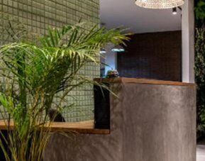 Reception area at 103 Wonderful House featuring a contemporary front desk, green tiled wall and lush indoor plants.