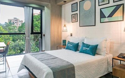 Bright guest room at Hotel Loft 32 featuring a comfortable bed, large windows overlooking greenery, workspace and contemporary décor.