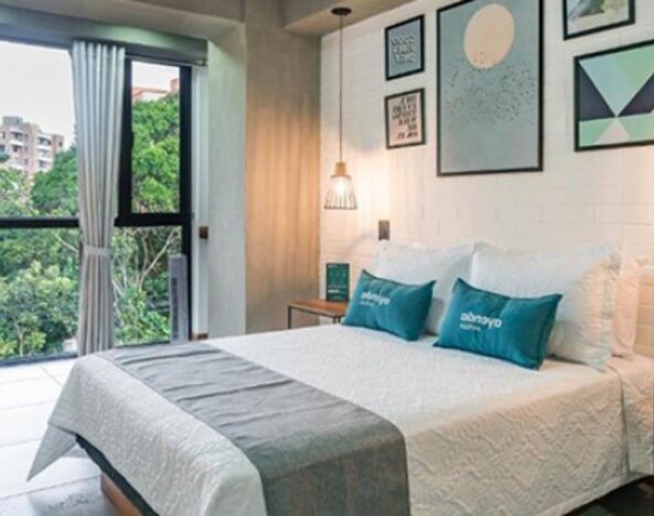 Bright guest room at Hotel Loft 32 featuring a comfortable bed, large windows overlooking greenery, workspace and contemporary décor.