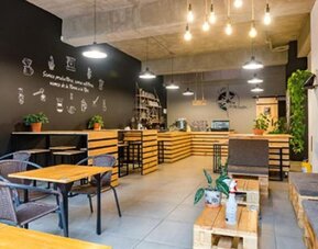 Café-style dining area at Hotel Loft 32 featuring wooden tables, lounge seating, greenery and modern lighting.