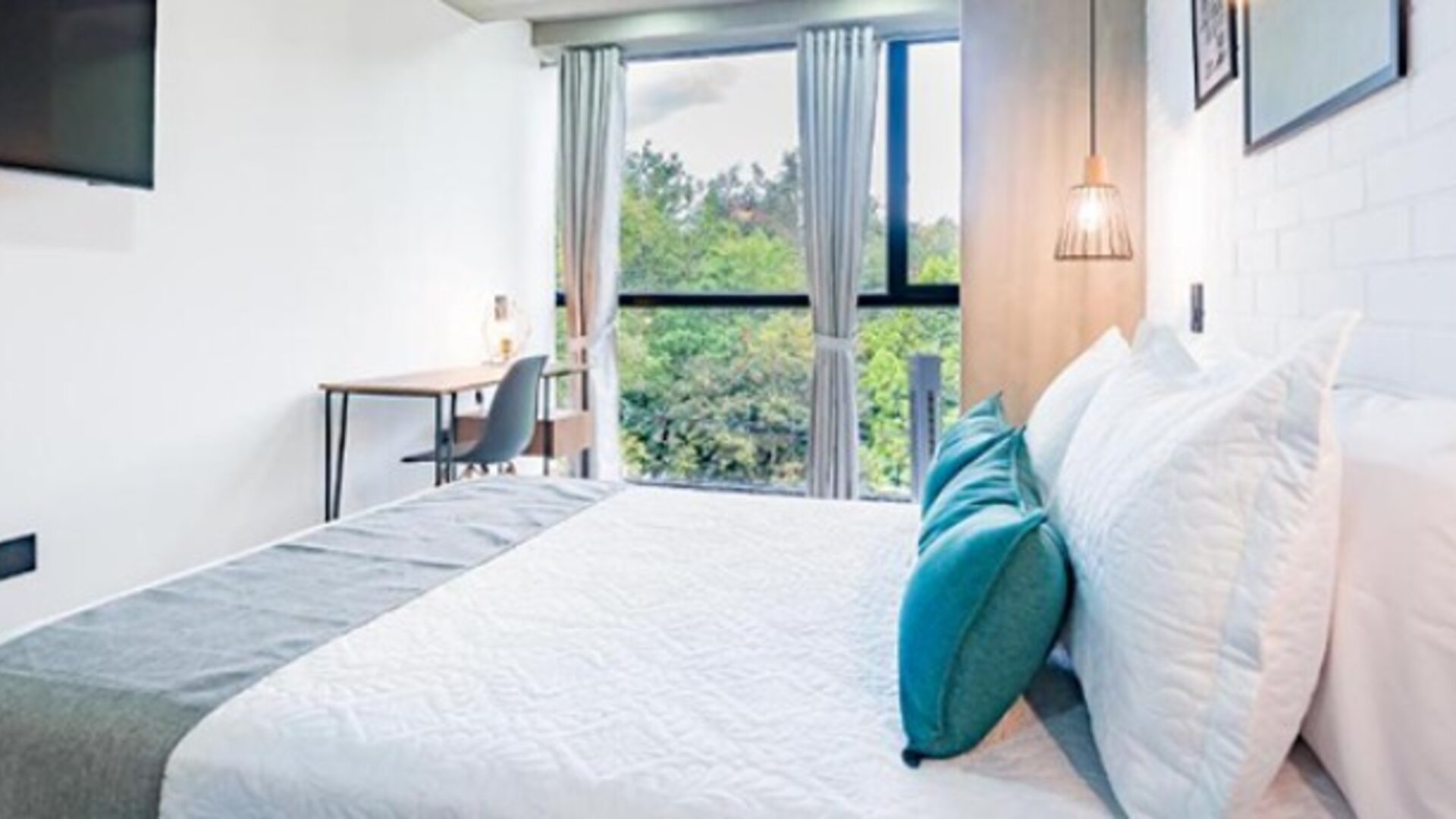 Bright guest room at Hotel Loft 32 featuring a comfortable bed, workspace and large window overlooking greenery.