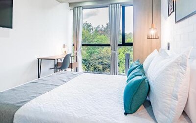 Bright guest room at Hotel Loft 32 featuring a comfortable bed, workspace and large window overlooking greenery.