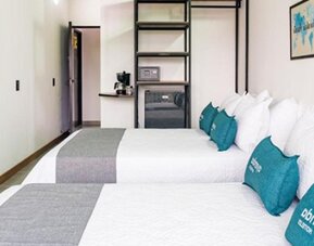 Spacious guest room at Hotel Loft 32 featuring two beds, teal accent cushions, a flat-screen TV and in-room storage.