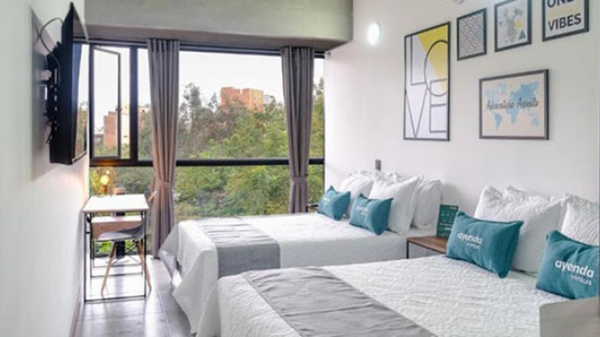 Guest room at Hotel Loft 32 featuring two beds, large windows, a workspace and colorful contemporary wall art.