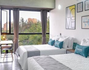 Guest room at Hotel Loft 32 featuring two beds, large windows, a workspace and colorful contemporary wall art.