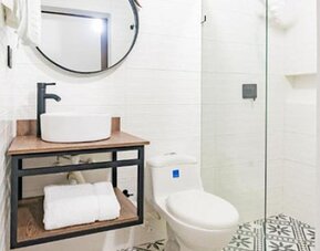 Modern bathroom at Hotel Loft 32 featuring a vessel sink, round mirror, toilet and glass-enclosed shower.