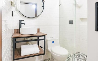 Modern bathroom at Hotel Loft 32 featuring a vessel sink, round mirror, toilet and glass-enclosed shower.