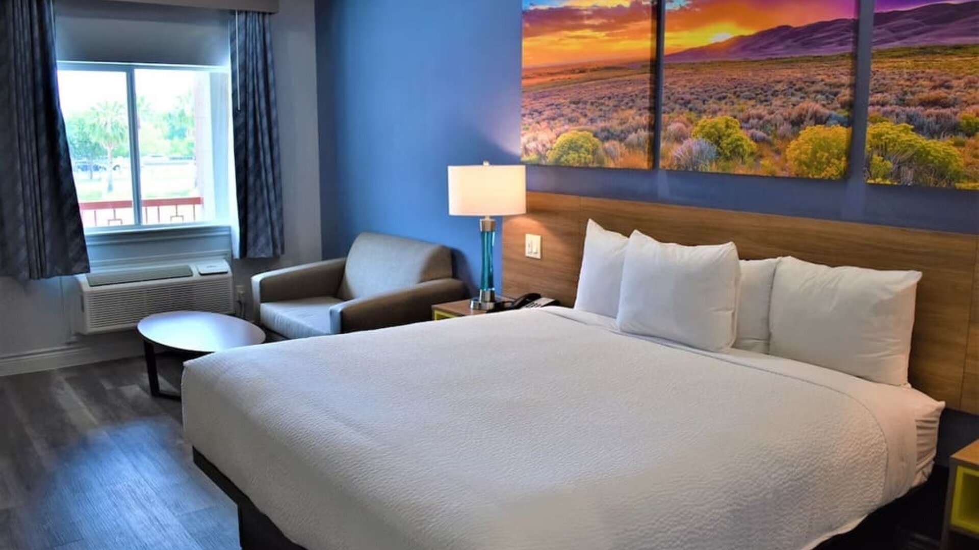 King room at Days Inn & Suites By Wyndham Downtown/University Of Houston featuring a king bed, seating area, window and colorful landscape artwork.