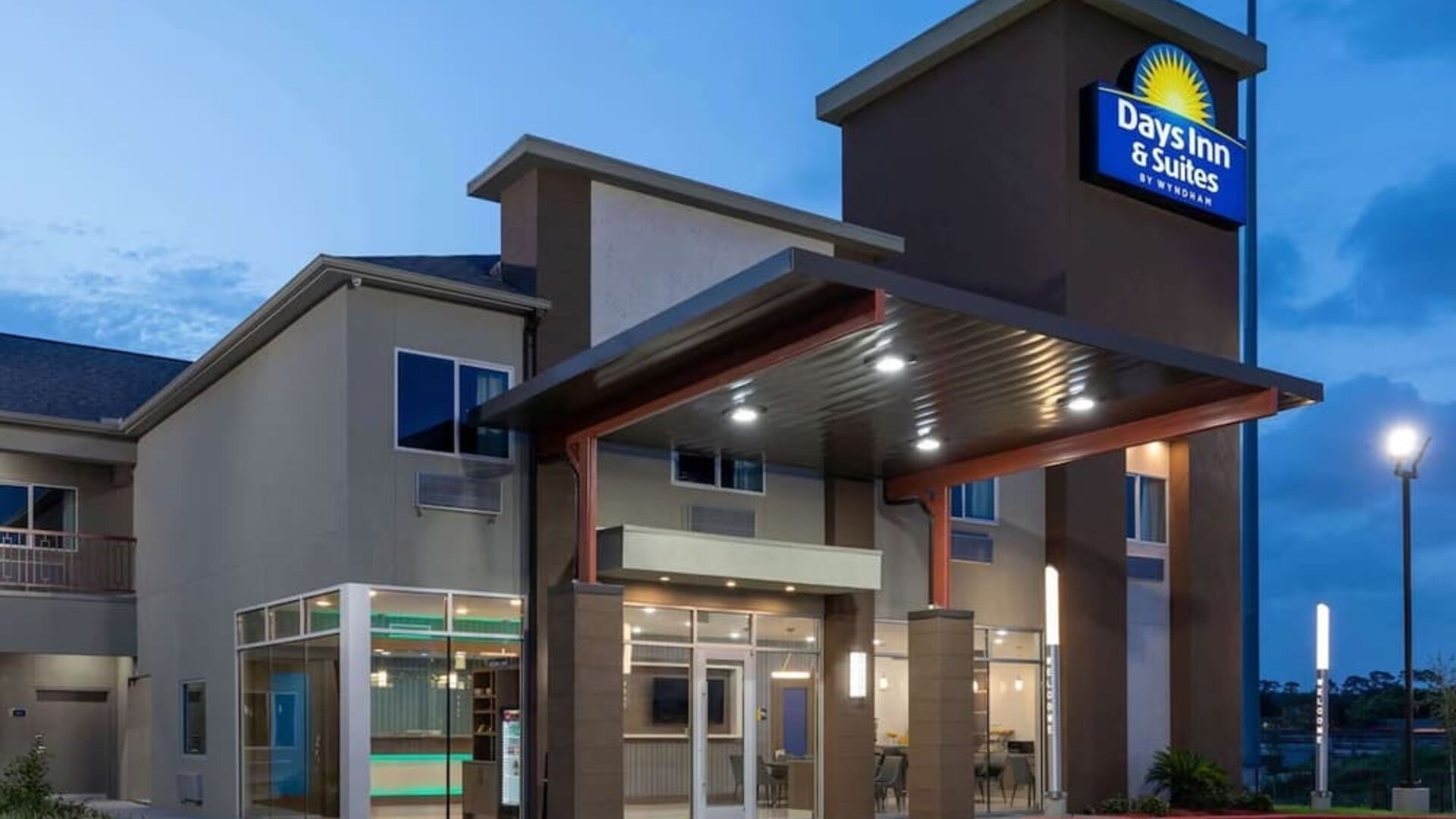 Front entrance of Days Inn & Suites By Wyndham Downtown/University Of Houston featuring a covered entrance and illuminated hotel signage.