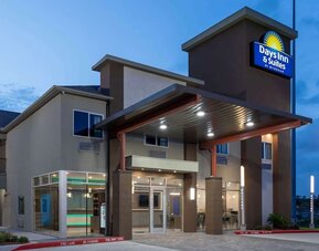Front entrance of Days Inn & Suites By Wyndham Downtown/University Of Houston featuring a covered entrance and illuminated hotel signage.