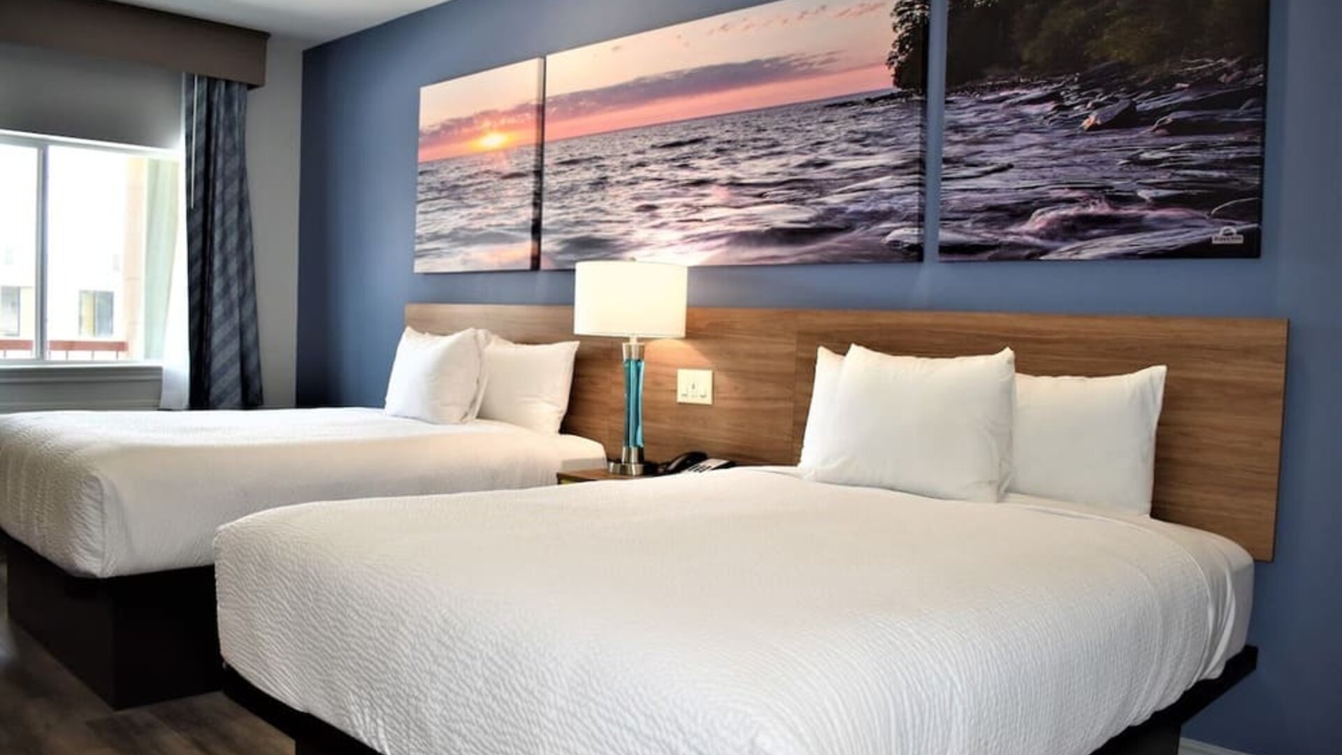 Guest room at Days Inn & Suites By Wyndham Downtown/University Of Houston featuring two beds, bedside lighting and scenic wall artwork.