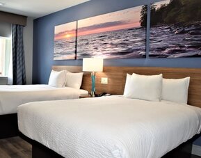 Guest room at Days Inn & Suites By Wyndham Downtown/University Of Houston featuring two beds, bedside lighting and scenic wall artwork.