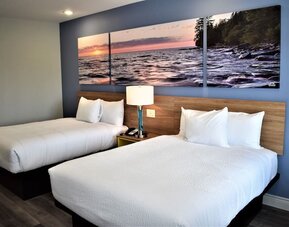 Guest room at Days Inn & Suites By Wyndham Downtown/University Of Houston featuring two beds and colorful scenic wall artwork.