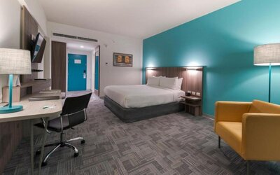 Guest room at Holiday Inn Lima Airport featuring a king bed, work desk, armchair, television and contemporary turquoise accent wall.