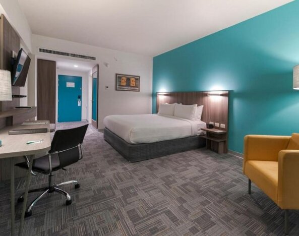 Guest room at Holiday Inn Lima Airport featuring a king bed, work desk, armchair, television and contemporary turquoise accent wall.