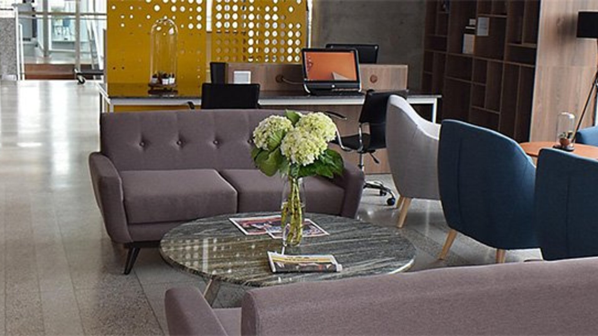 Lobby seating area at Holiday Inn Lima Airport featuring modern sofas, blue armchairs, a glass coffee table and fresh flowers.