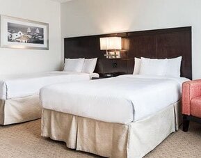 Double guest room at Courtyard Panama Metromall featuring two beds, an armchair, side table and contemporary dark wood headboard.