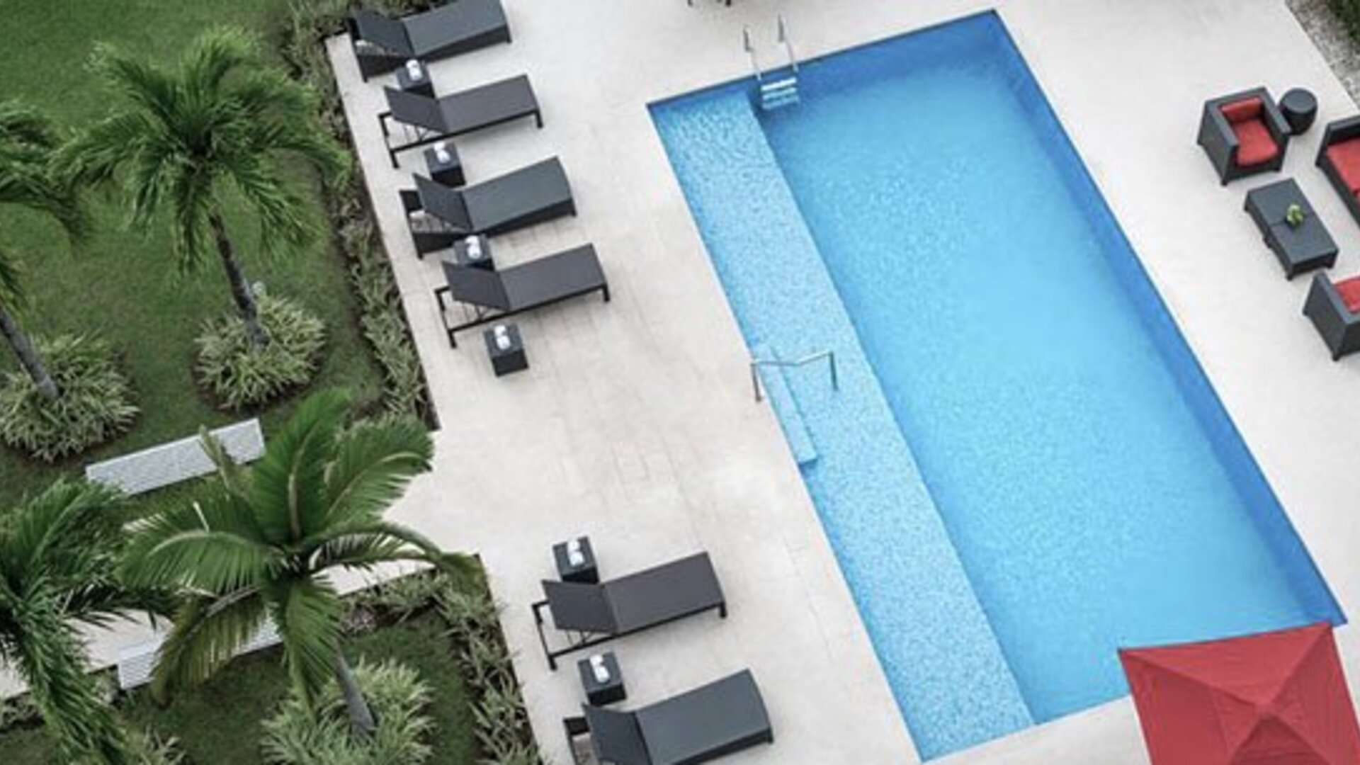 Overhead view of the outdoor pool at Courtyard Panama Metromall featuring sun loungers, patio seating and surrounding greenery.