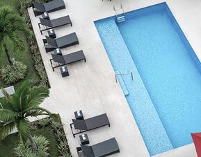 Overhead view of the outdoor pool at Courtyard Panama Metromall featuring sun loungers, patio seating and surrounding greenery.