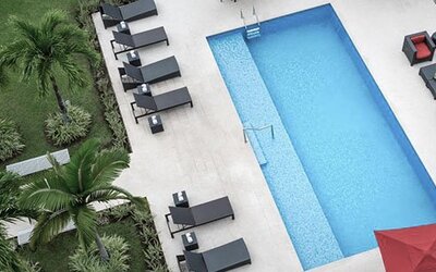 Overhead view of the outdoor pool at Courtyard Panama Metromall featuring sun loungers, patio seating and surrounding greenery.