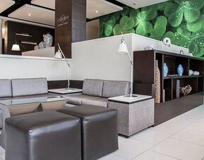 Lobby seating area at Courtyard Panama Metromall featuring sofas, ottomans, individual reading lamps and a green feature wall.