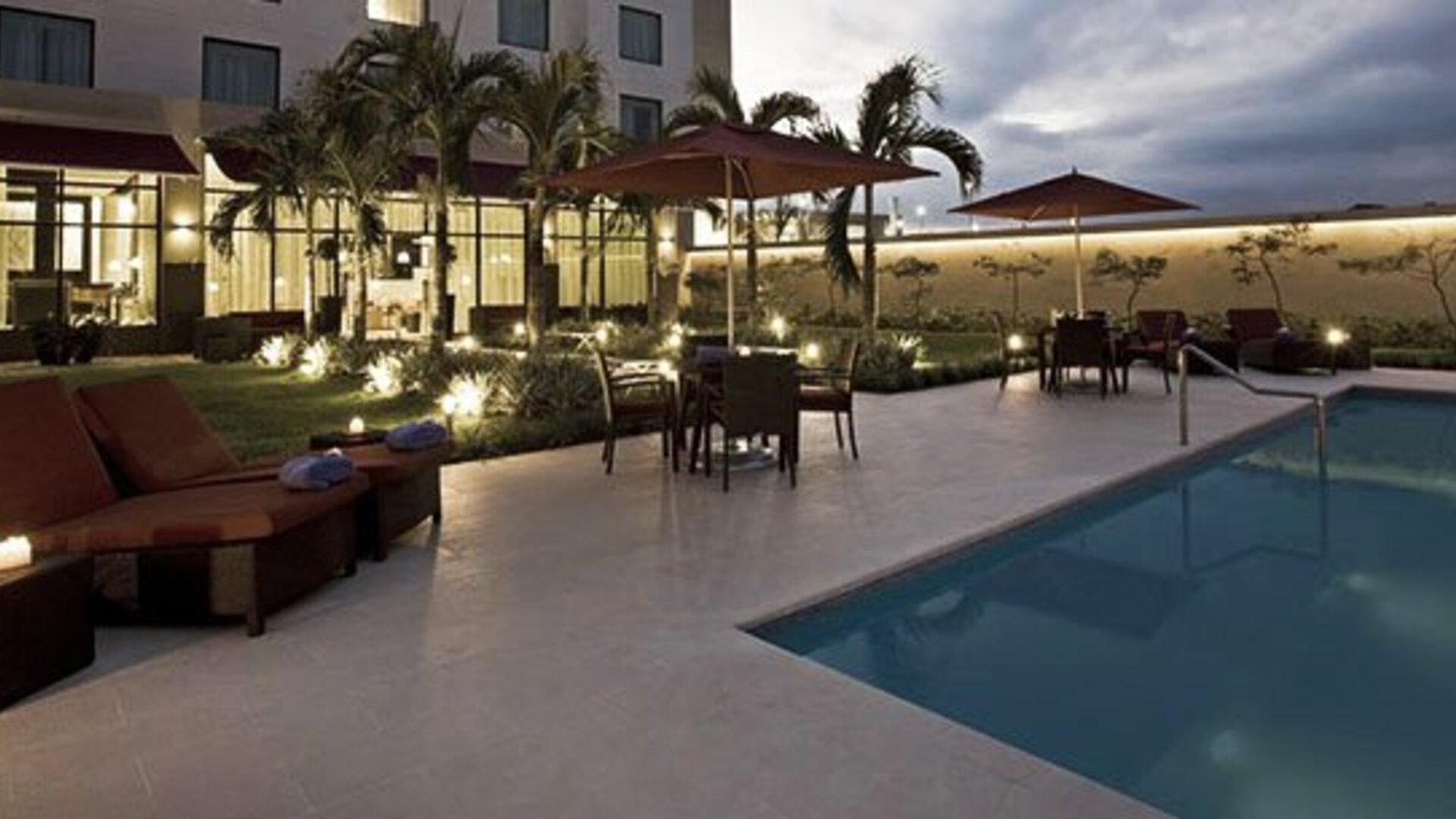 Outdoor pool at Courtyard Panama Metromall featuring lounge chairs, umbrellas, patio seating and landscaped surroundings.