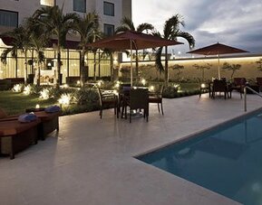 Outdoor pool at Courtyard Panama Metromall featuring lounge chairs, umbrellas, patio seating and landscaped surroundings.