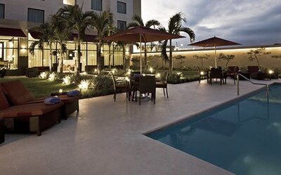 Outdoor pool at Courtyard Panama Metromall featuring lounge chairs, umbrellas, patio seating and landscaped surroundings.