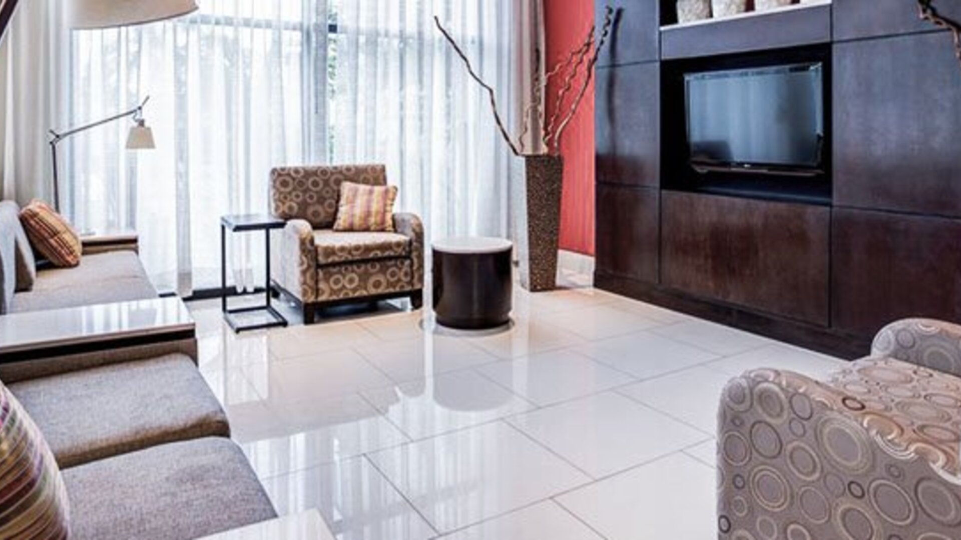 Lounge area at Courtyard Panama Metromall featuring sofas, patterned armchairs, modern lighting and a wall-mounted television.
