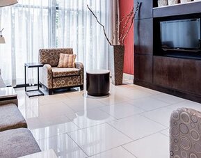 Lounge area at Courtyard Panama Metromall featuring sofas, patterned armchairs, modern lighting and a wall-mounted television.