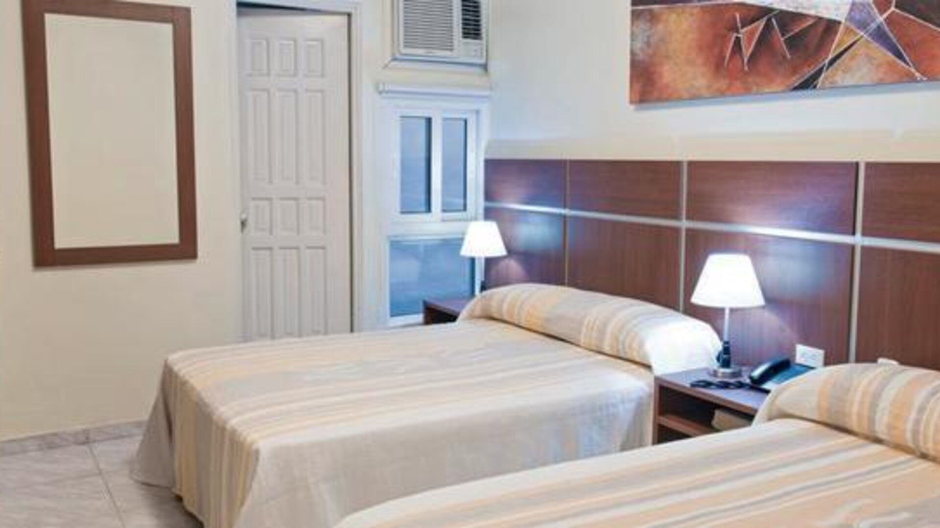 Twin guest room at Hotel Benidorm featuring two beds, bedside lamps, wooden furnishings and a wall-mounted air-conditioning unit.