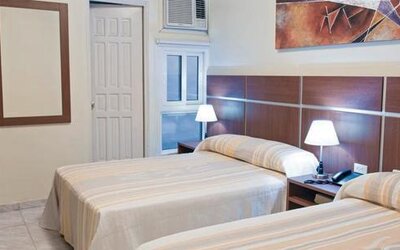 Twin guest room at Hotel Benidorm featuring two beds, bedside lamps, wooden furnishings and a wall-mounted air-conditioning unit.