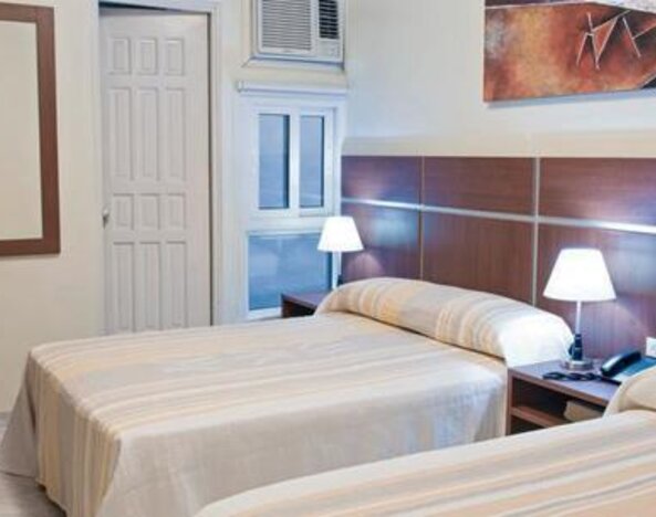 Twin guest room at Hotel Benidorm featuring two beds, bedside lamps, wooden furnishings and a wall-mounted air-conditioning unit.