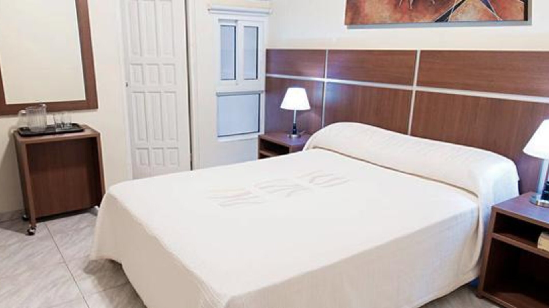 Guest room at Hotel Benidorm featuring a double bed, bedside lamps, wooden furnishings and a small refreshment station.
