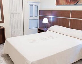 Guest room at Hotel Benidorm featuring a double bed, bedside lamps, wooden furnishings and a small refreshment station.