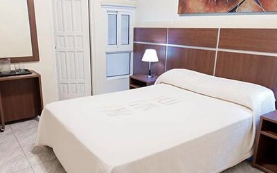 Guest room at Hotel Benidorm featuring a double bed, bedside lamps, wooden furnishings and a small refreshment station.