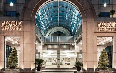 Main entrance of Hotel Marquis Reforma featuring an illuminated arched glass canopy and landscaped planters.