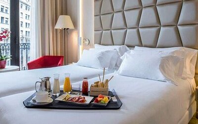 Guest room featuring a large bed, breakfast tray, red accent chair and natural light from the balcony doors at NH Collection Barcelona Pódium.