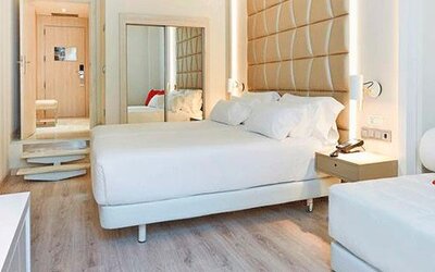 Bright guest room featuring a large bed, sofa, red accent cushion and contemporary furnishings at NH Collection Barcelona Pódium.