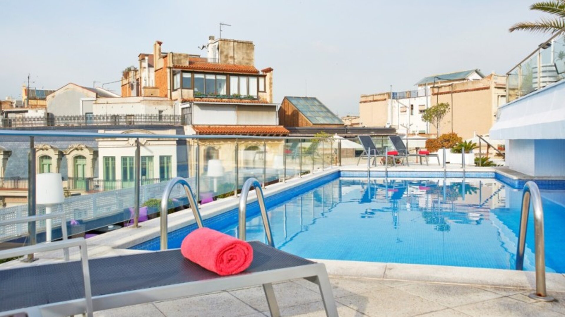 Rooftop swimming pool featuring sun loungers and surrounding city views at NH Collection Barcelona Pódium.