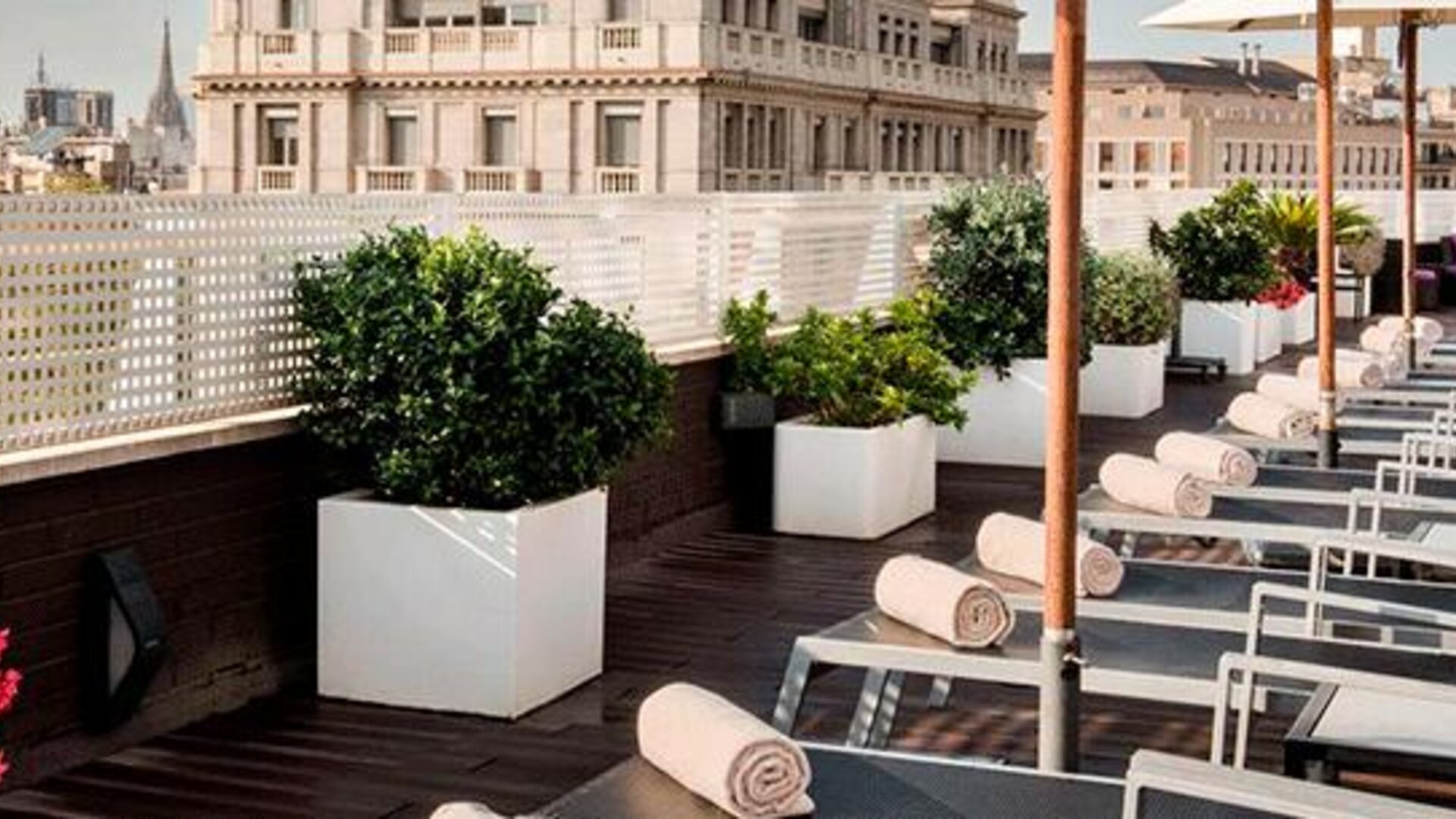 Rooftop terrace featuring sun loungers, umbrellas, planters and city views at NH Collection Barcelona Pódium.