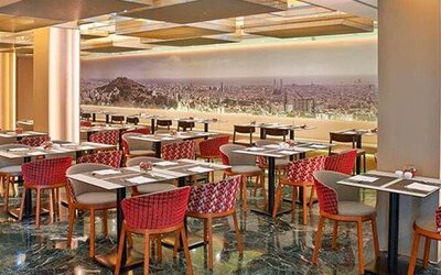 Spacious restaurant featuring dining tables, red patterned chairs and a panoramic city mural at NH Collection Barcelona Pódium.