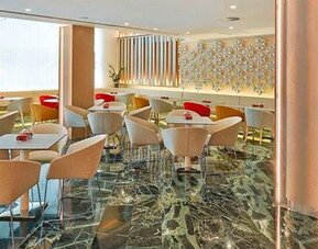 Modern dining area featuring tables, upholstered chairs and a bar counter at NH Collection Barcelona Pódium.