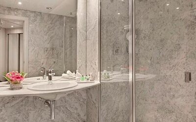 Marble bathroom featuring a sink, large mirror and glass-enclosed shower at NH Collection Barcelona Pódium.