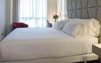 Modern guest room featuring a large bed, upholstered headboard, bedside lighting and natural light at NH Collection Barcelona Pódium.