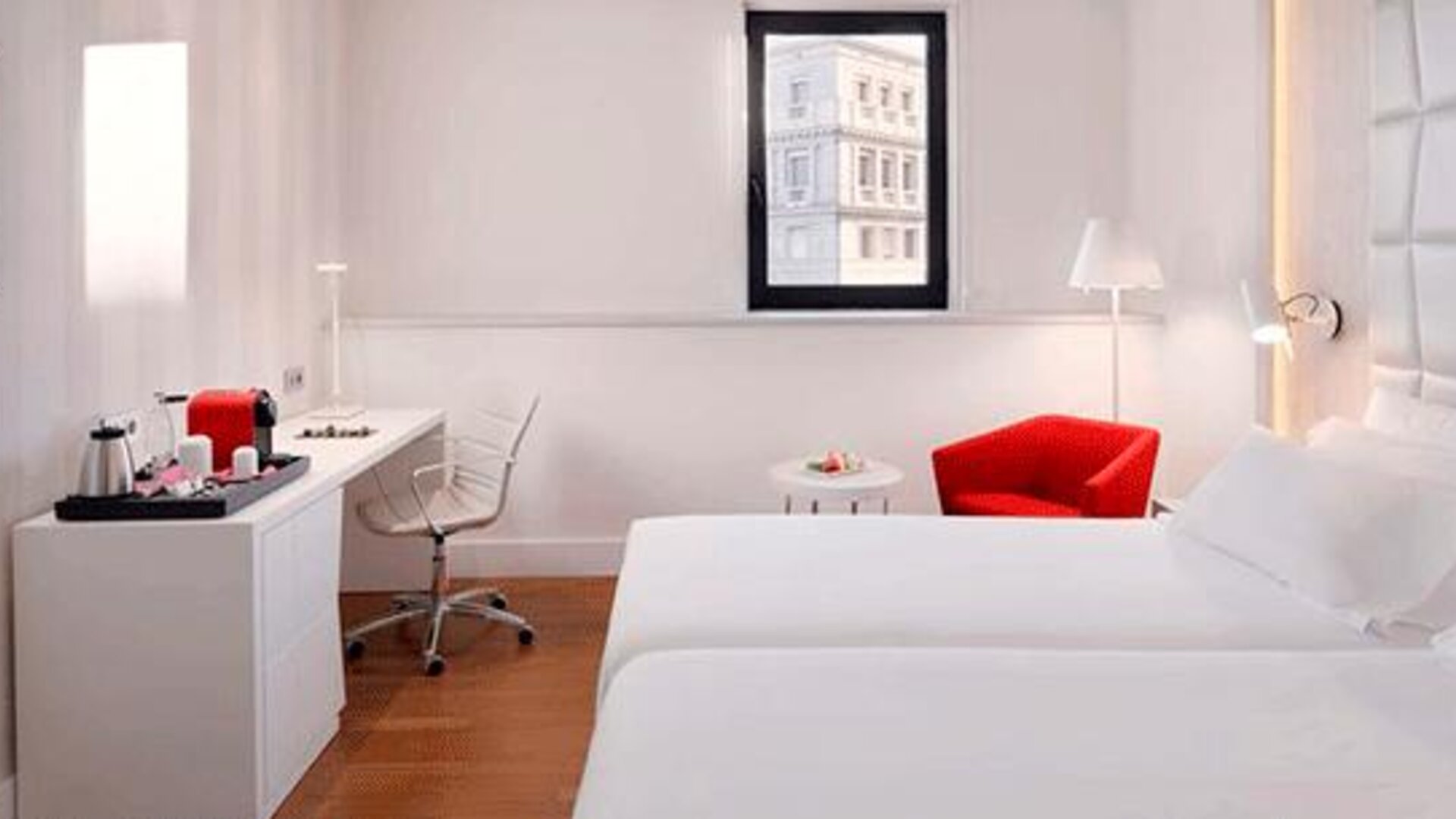 Contemporary guest room featuring two beds, a work desk, red accent chair and wall-mounted television at NH Collection Barcelona Pódium.